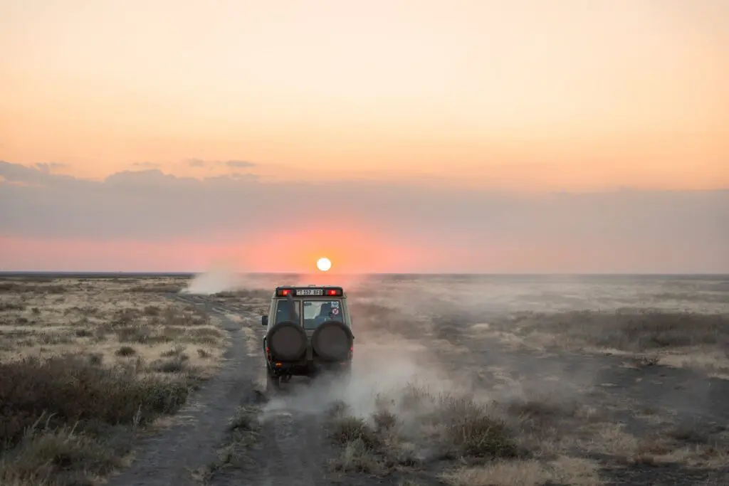 safari jeep driving through dusty plains at sunset