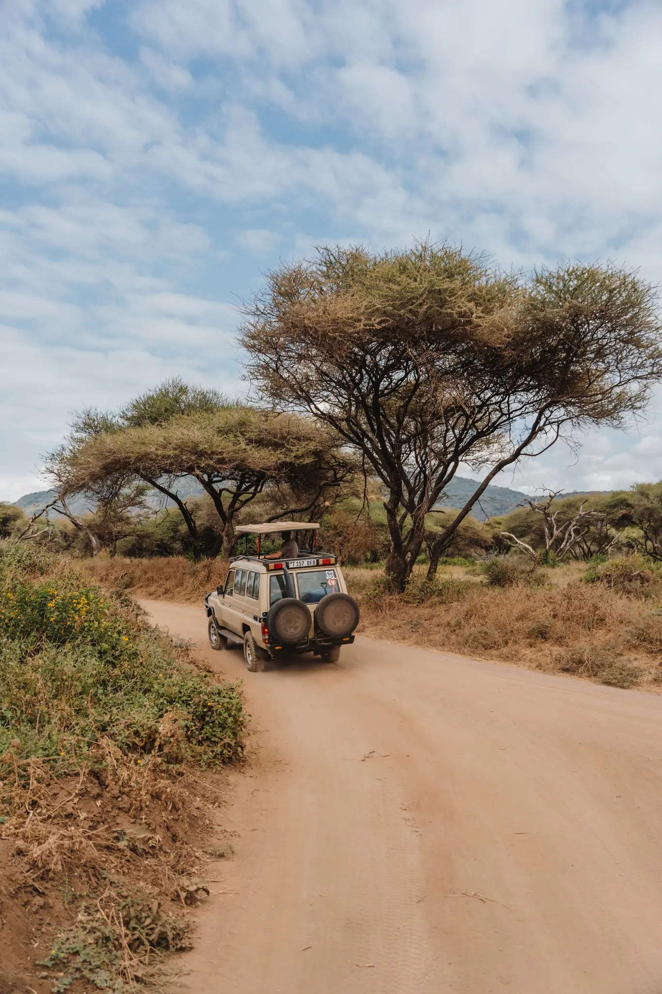 safari jeep driving on dirt road in tanzania