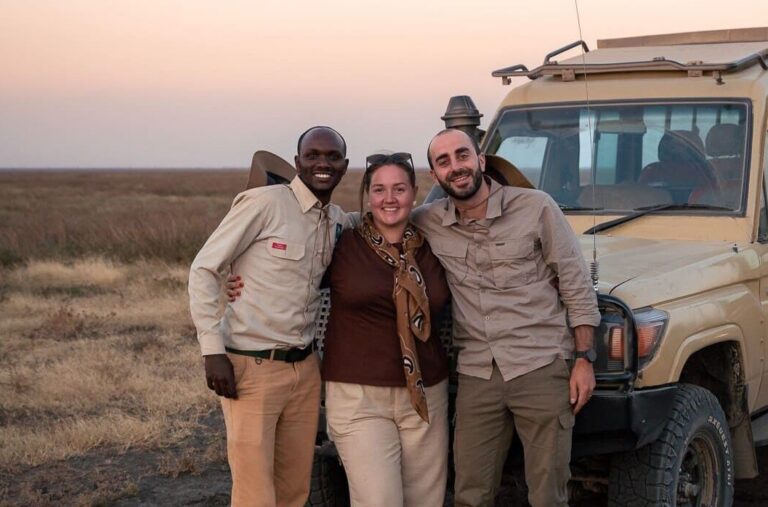 three people smiling in front of a safari jeep at sunset